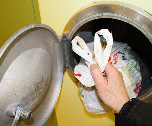 En person slänger ner sina sopor i ett sopnedkast, Skåne